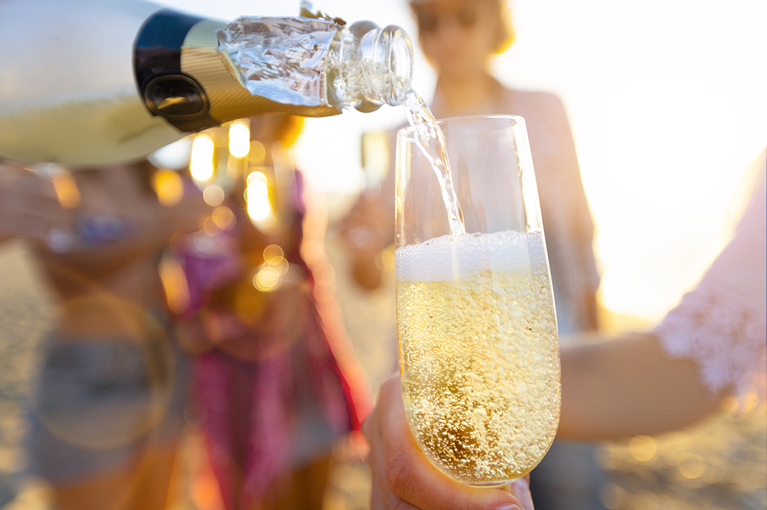 Pouring a glass of champagne with people partying in the background.